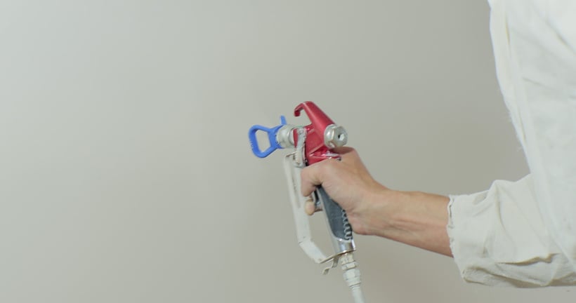 Airless spray painting. Close-up of a worker hand holds an electric spray gun and paints the wall.