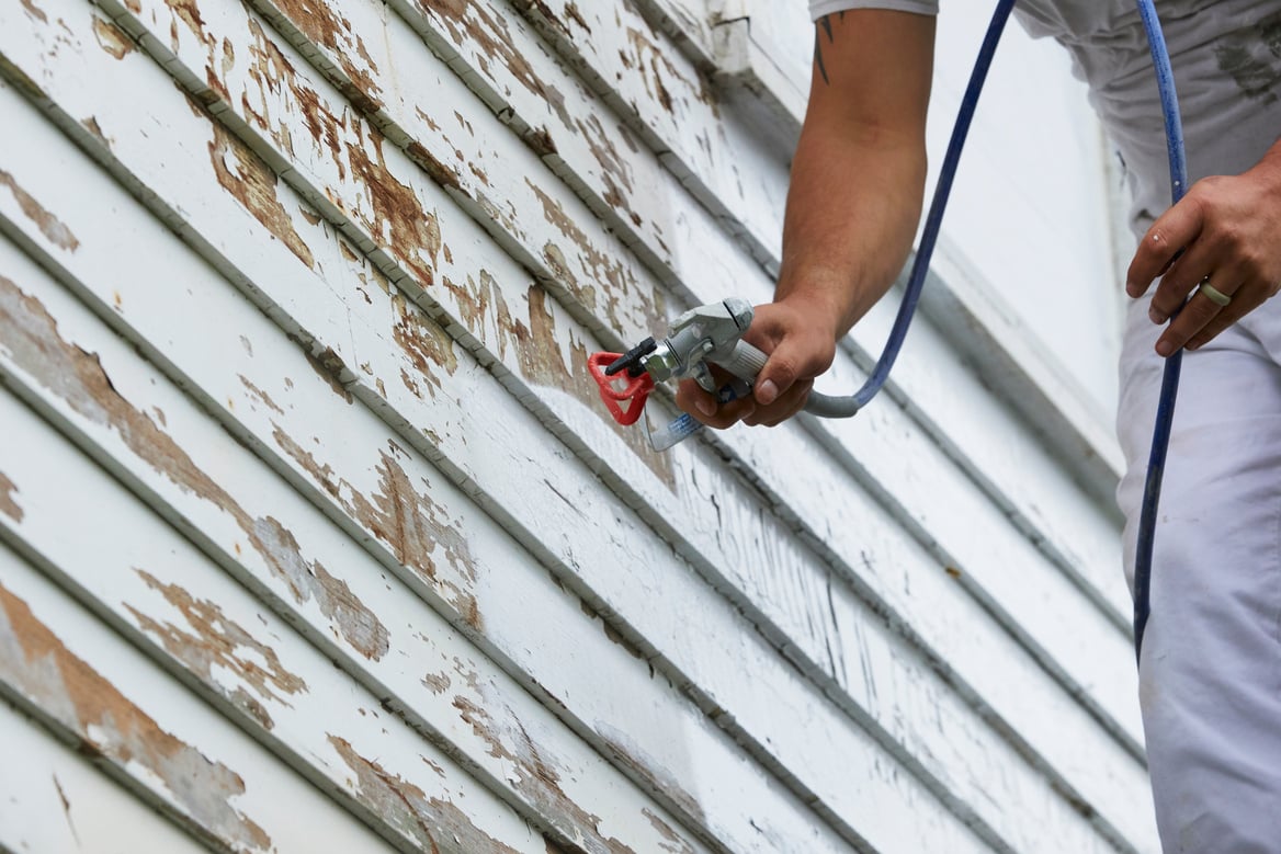 Male painting home with airless paint sprayer.